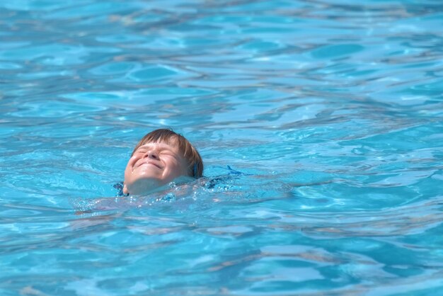 Child girl learns to swim Funny face with closed eyes on bright blue rippled water surface