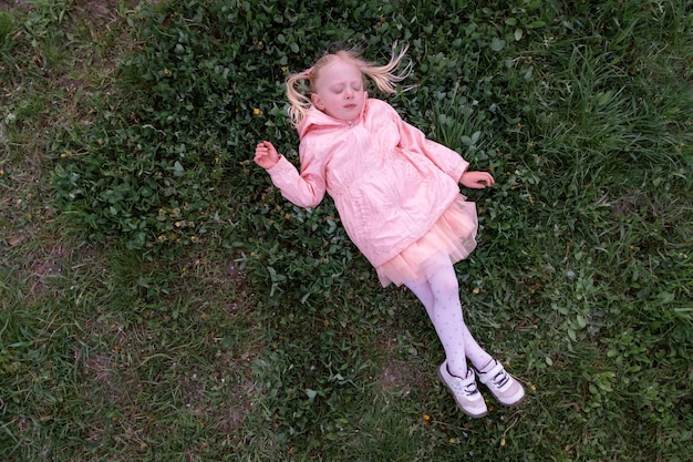 Child girl lying on the grass Preschool girl in pink jacket lay down to rest in the green meadow Top view