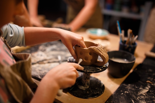 陶器工房で赤い粘土からカップを作る子供の女の子。
