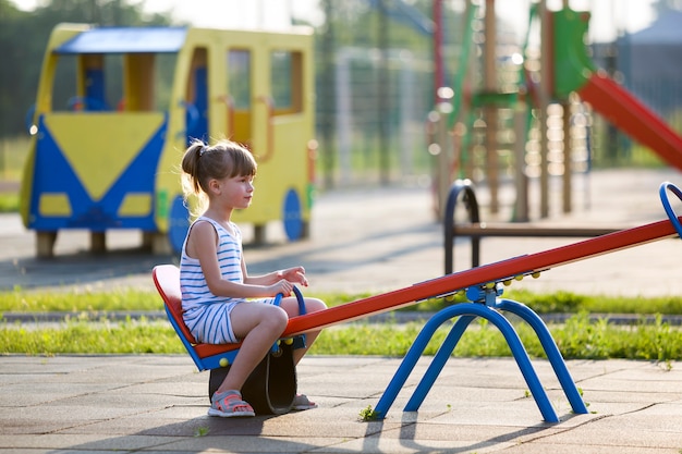 Child girl outdoors on see-saw swing on sunny summer day.