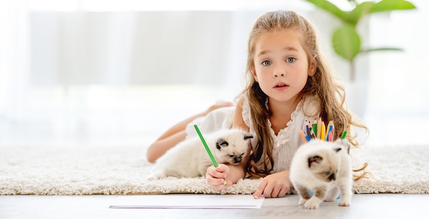 Картина детской девочки с котятами тряпичной куклы на полу. маленькая женщина рисует красочными карандашами и домашних животных котенка рядом с ней дома