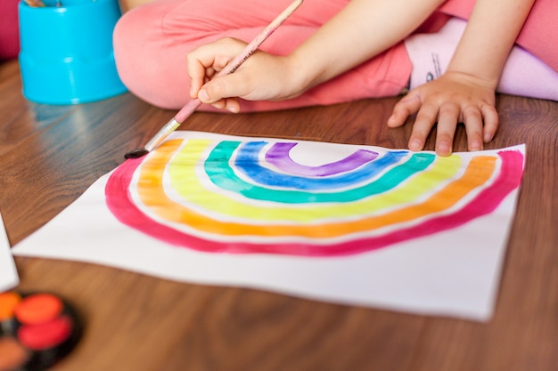 child girl paints a rainbow on paper indoor