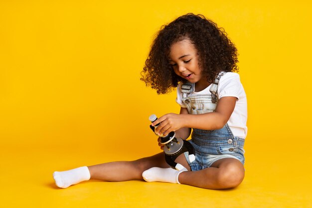 Child girl playing with microscope yellow background