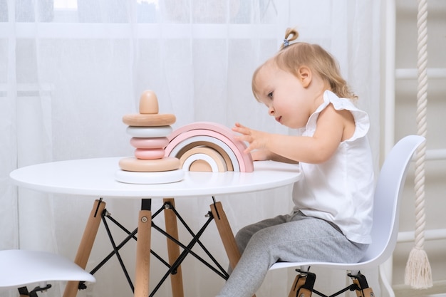Ребенок девочка играет с деревянными игрушками за столом. Маленькая милая девочка с натуральными игрушками.
