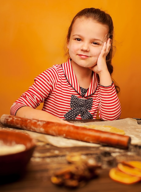 子供、女の子は木製の背景にクッキーの生地を準備します