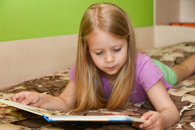 Child girl reading book in bed at home.