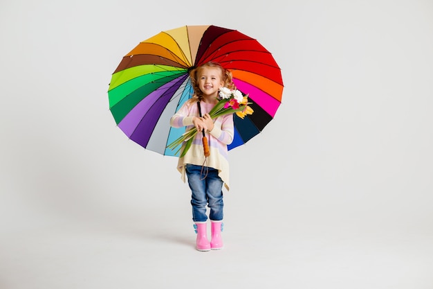 Child girl in rubber boots holding a multicolored umbrella