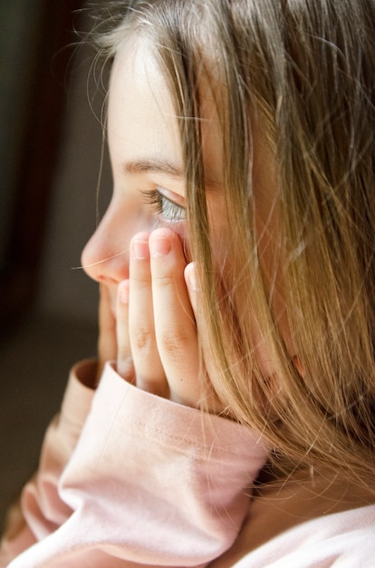 Child girl sad profile face close up with hands on cheek.