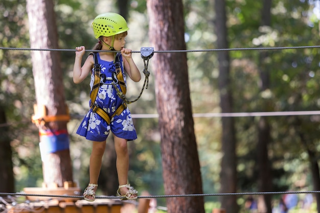 Ragazza del bambino in imbracatura di sicurezza e casco sul modo della corda