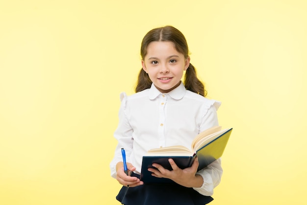 Child girl school uniform clothes hold book and pen Girl cute write down idea notes Notes to remember Write essay or notes Personal schedule Making notes Child school uniform kid doing homework