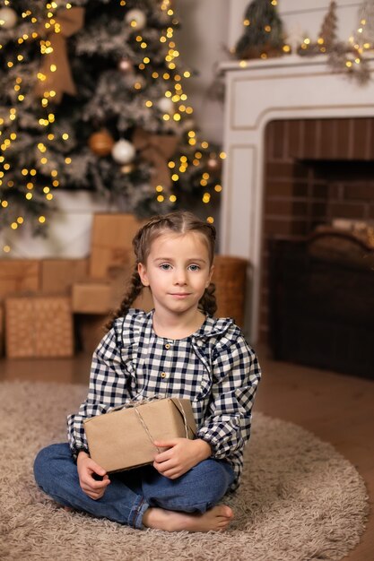 어린 소녀는 크리스마스 트리 바닥에 앉아 새해 선물을 엽니다