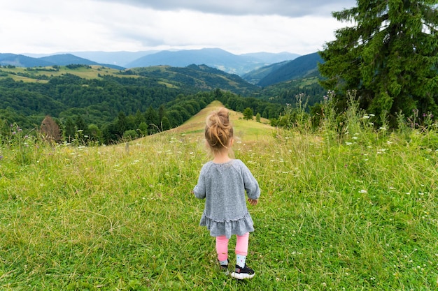 Child girl standing on peak and looking at mountains. Summer outdoor landscape