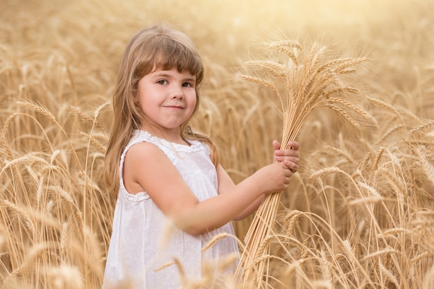 Child girl standing in a wheat field and holding wheat spikelets in her hands, smiling, concept