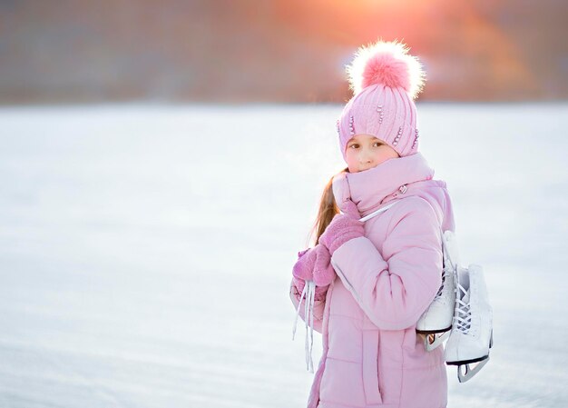 子供の女の子は冬に通りに立ち、スケートを持っています