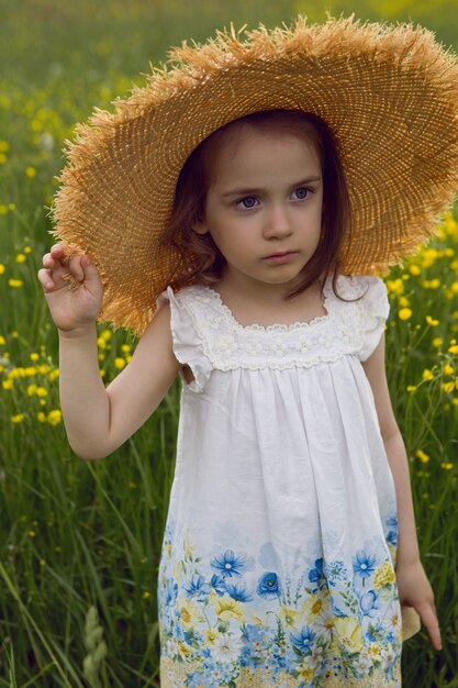 Child girl in a straw hat and a dress with flowers stands on a yellow field