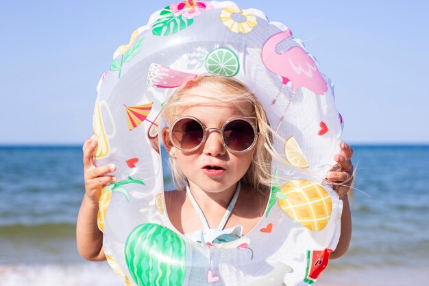 Child girl in sunglasses looks through an inflatable circle on the beach