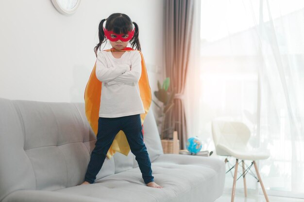 Child girl in a super hero costume with mask and red cloak at home