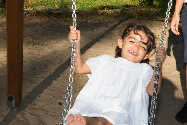 Ragazza del bambino che oscilla nel parco giochi con la mano della madre per spingere