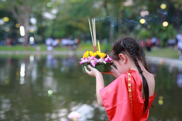 Ребенок девочка в тайском платье держит Кратонг, чтобы отпраздновать фестиваль в Таиланде