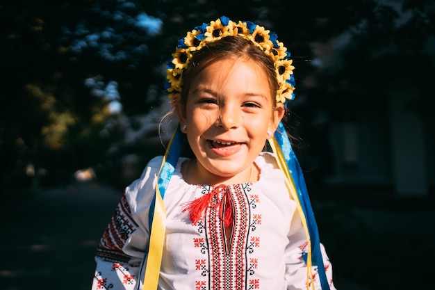 Foto ragazza bambina in abiti tradizionali ucraini e corona di fiori sta pregando all'aperto alla luce del sole