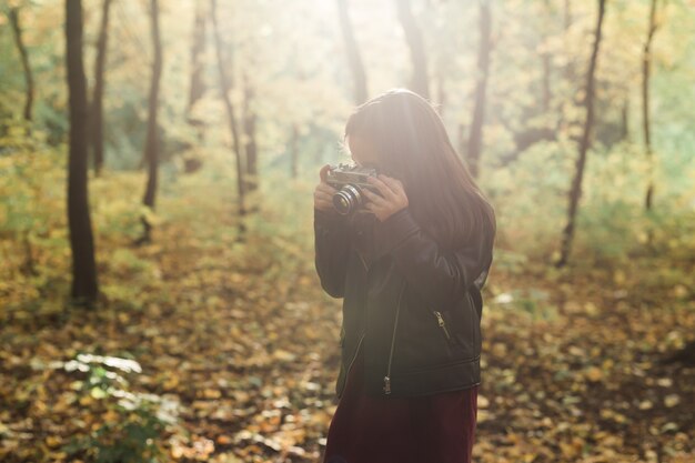 秋の自然の中で昔ながらのカメラを使用して子供の女の子。写真家、秋のシーズンとレジャーのコンセプト。