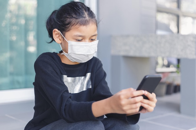 Child girl wear face mask during COVID-19 outbreak using smartphone study online. little girl chatting learning online.