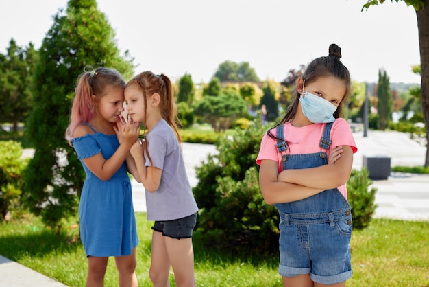 保護のためのマスクを身に着けている子供の女の子と他の子供たちは彼女の屋外を見ています。