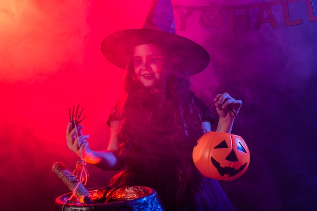 Foto strega della ragazza del bambino che prepara una pozione nel calderone alle feste di halloween