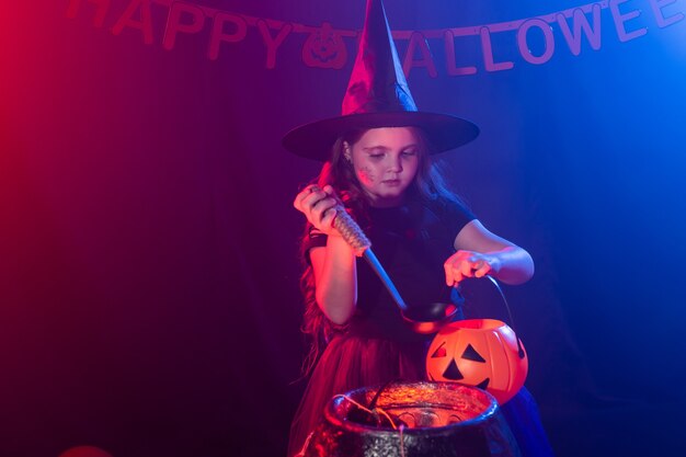 Child girl witch preparing a potion in the cauldron at halloween holidays