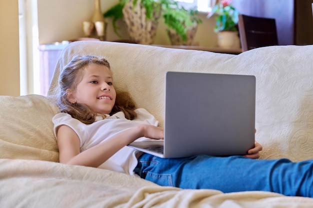 Child girl with laptop at home on the couch