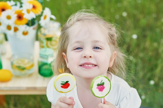 レモネードを持つ子供の女の子。テーブルの上のレモネードとデイジーの花。居心地の良い朝。