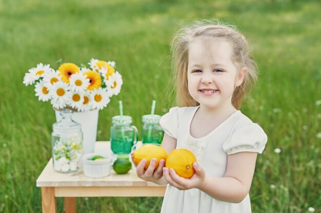 Child girl with lemonade. Lemonade and daisy flowers on table.