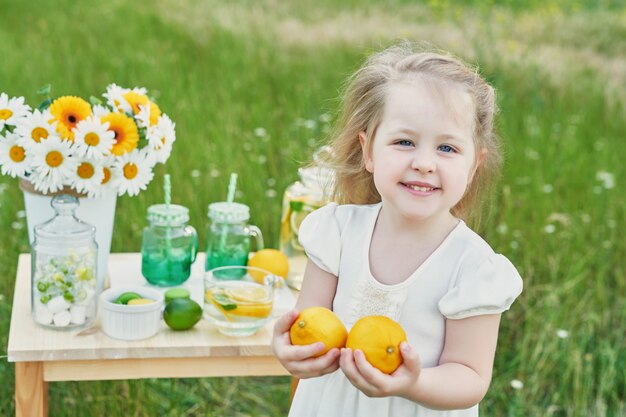 Child girl with lemonade. Lemonade and daisy flowers on table.