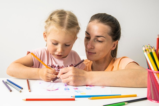 Child girl with mom draw with colored pencils on white paper