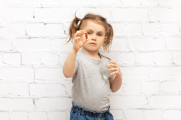 Ragazza del bambino con la pillola a portata di mano e un bicchiere d'acqua pillole e vitamine per i bambini