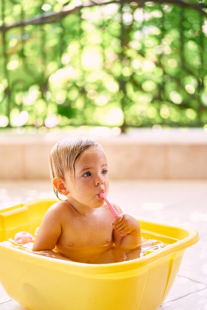 子供は水を入れたボウルに座って歯ブラシをかじる