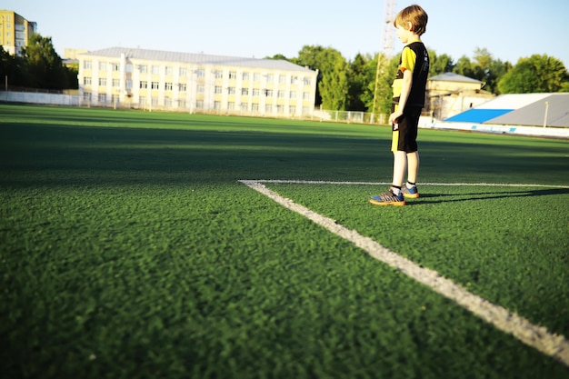 그 아이는 경기장에서 스포츠를 하러 간다 소년은 축구를 하기 전에 훈련하고 있다