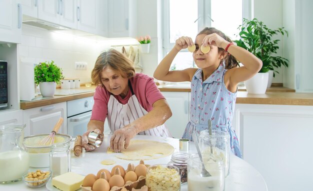 Child and grandmother in the kitchen bakes prepares the dough in the kitchen Selective focus Food