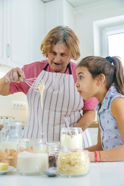 Ребенок и бабушка на кухне пекут, готовят тесто на кухне Избирательный фокус
