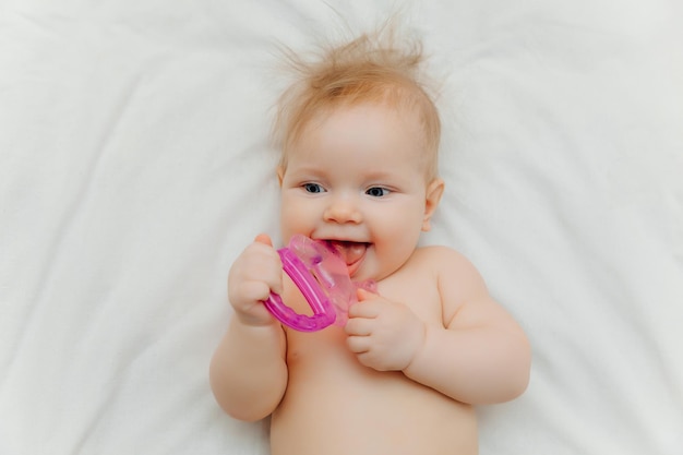 The child grows the first tooth Smiling baby 6 months old chewing teether in bed closeup