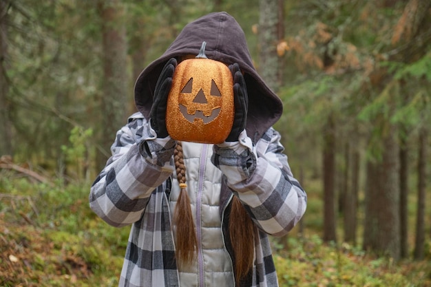 Child in halloween costume holding a decorative lantern pumpkin in front of his face
