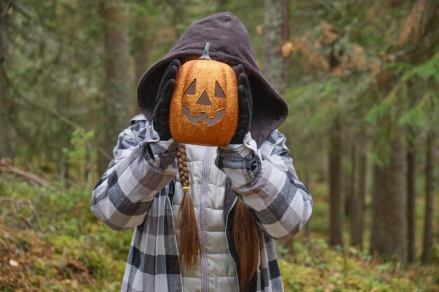 Child in halloween costume holding a decorative lantern pumpkin in front of his face