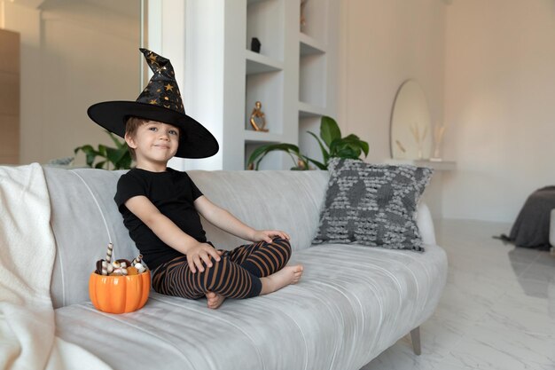 Photo a child in a halloween costume sits with pumpkin pot full of candies high quality photo