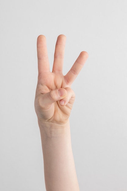 Child hand counting and showing three fingers against white and gray background