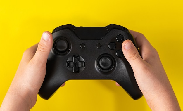 Child hand holding black game controller on yellow surface