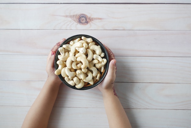 Child hand holding a bowl of cashew nut on table with copy space