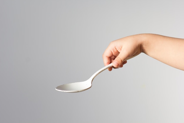 Child hand holding white spoon in right hand trying to hold it in right way on the white background