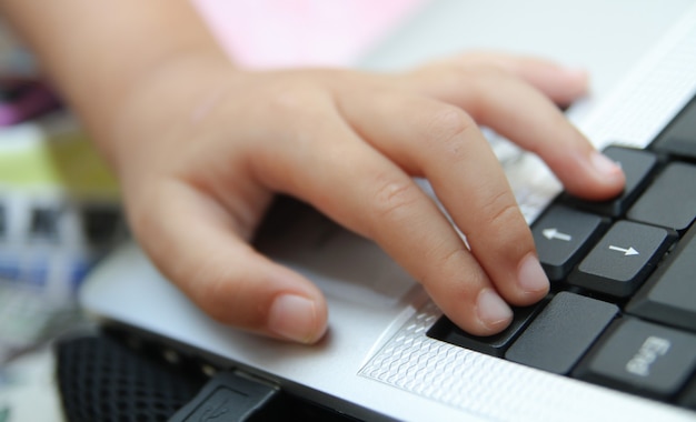 Рука ребенка держит компьютерную мышь или клавиатуру. Ребенок учится онлайн и играет дома на компьютере. Концепция школы, образования, игры и технологии.