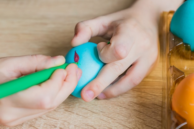 Mano del bambino che dipinge l'uovo di pasqua con il pennarello.