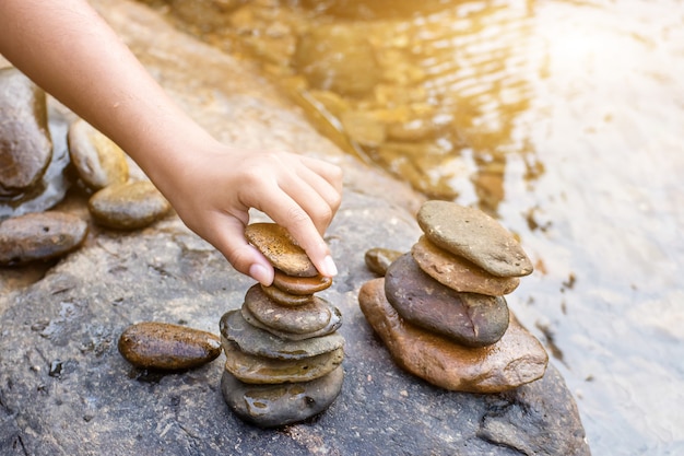 Child hand placing a rock stacks on top of a cairn on creek,Blurred background.